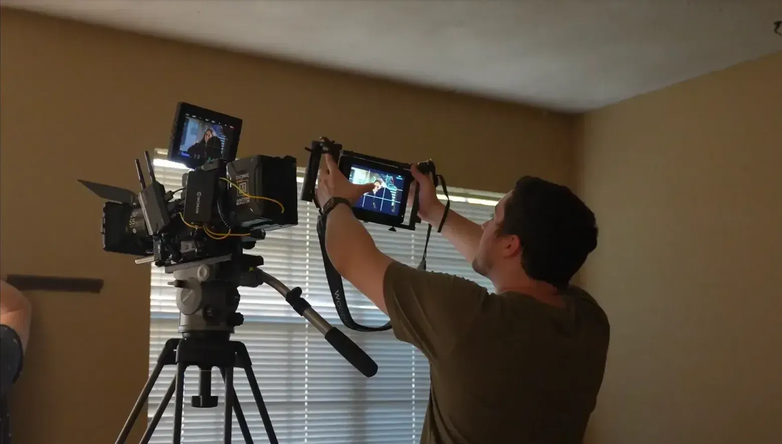 Videographer fine-tunes a cinema camera setup while checking a handheld director's monitor